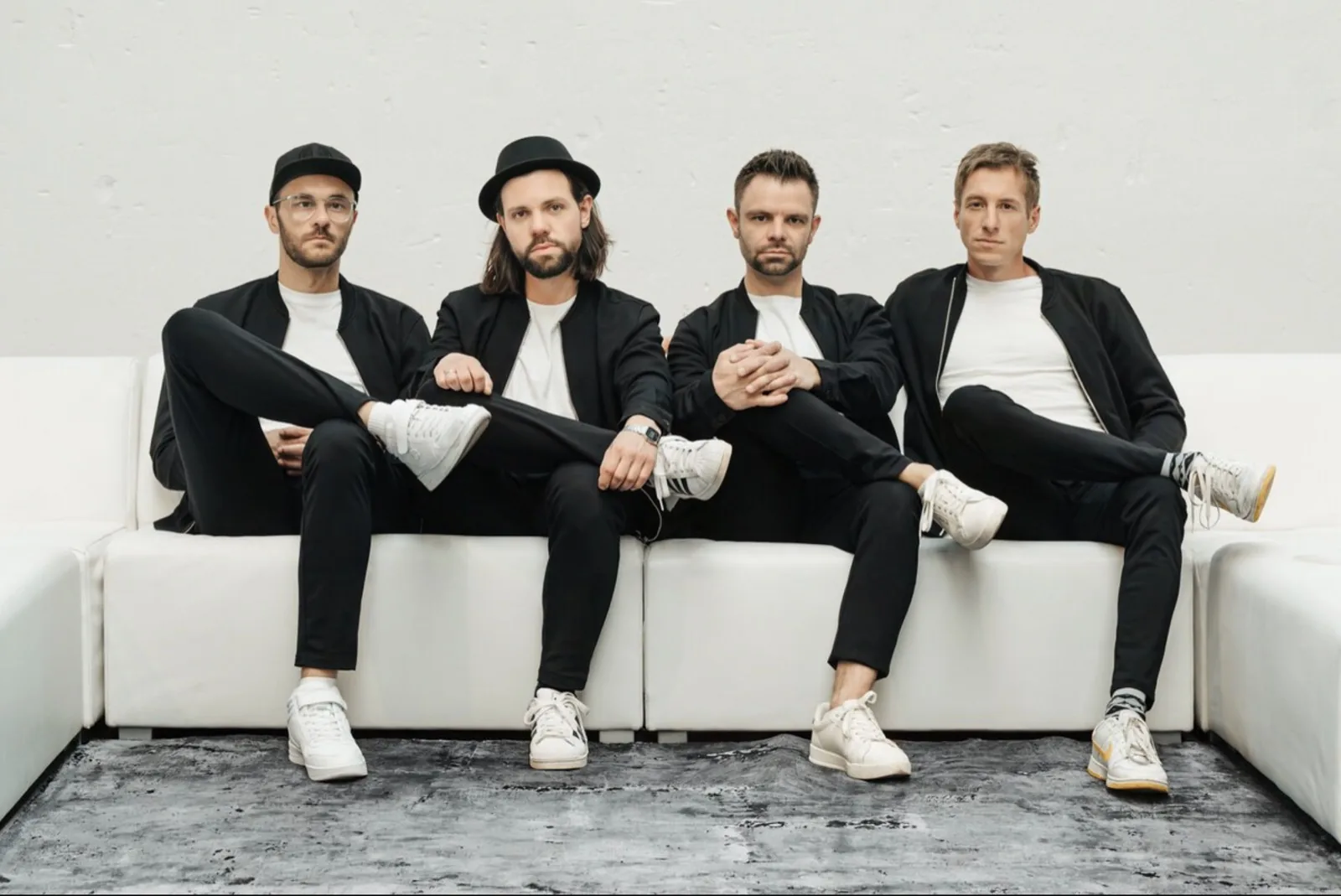 Die vier Musiker der Eventband GOODBEATS in schwarzen Sakkos und weißen Shirts nebeneinander auf einem weißen Sofa