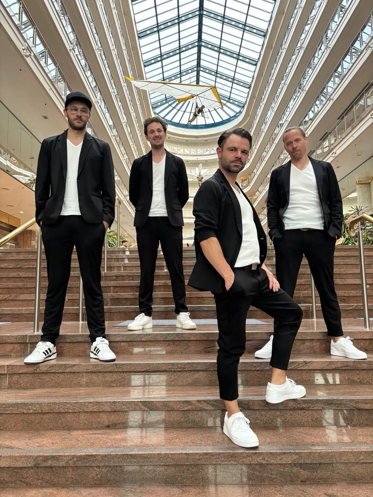 Die vier Musiker der GOODBEATS auf einer breiten Treppe in einem verglasten Atrium